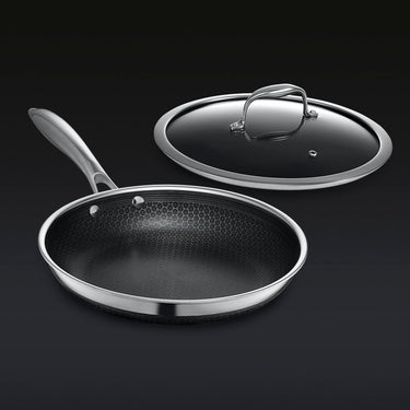 Hybrid stainless steel frying pan with matching glass lid on dark background