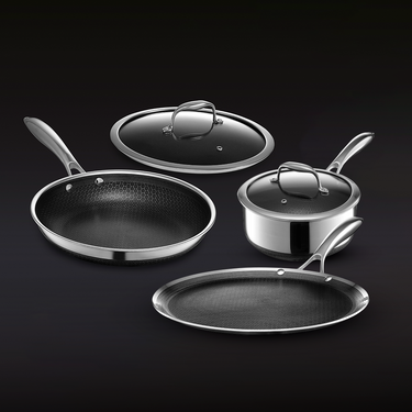 Stainless steel cookware set with pans, saucepan, and glass lids on dark background